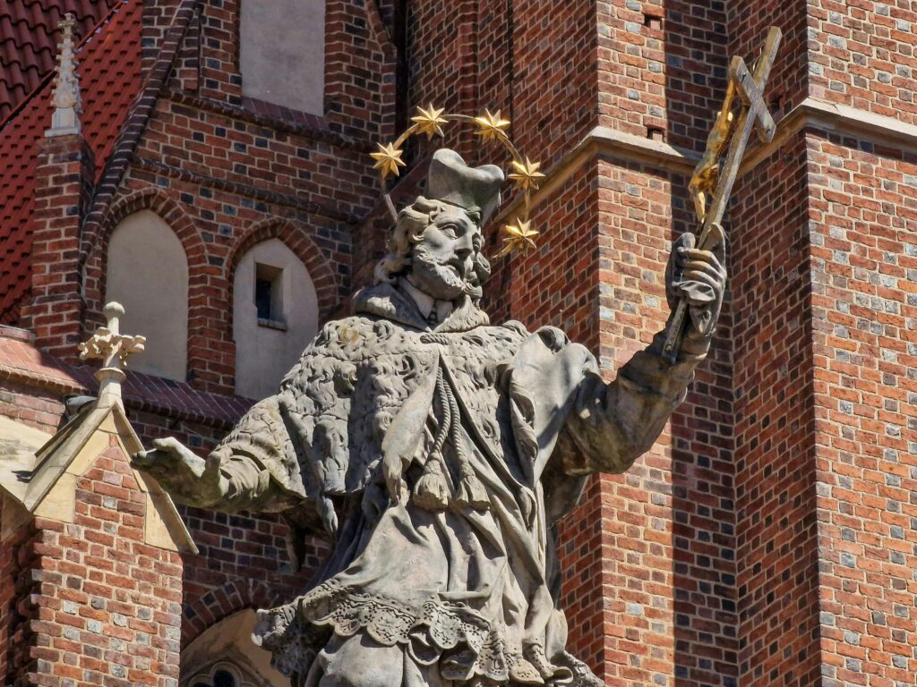 Close-up of St. John Nepomuk statue against brick church in Wrocław, Poland.