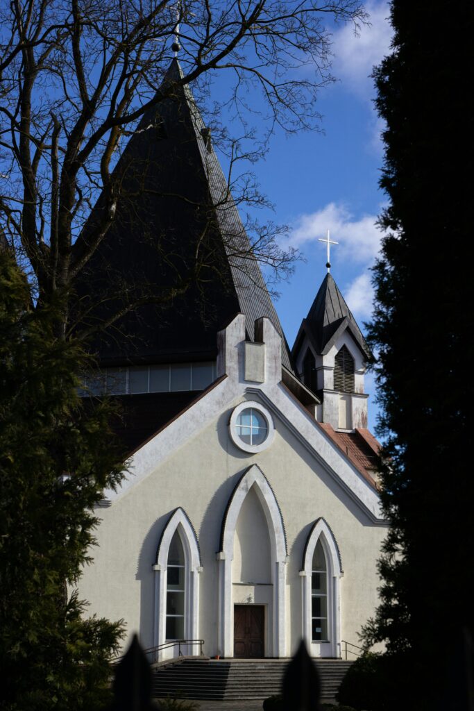 A beautiful Gothic style church exterior under a clear blue sky, surrounded by trees.